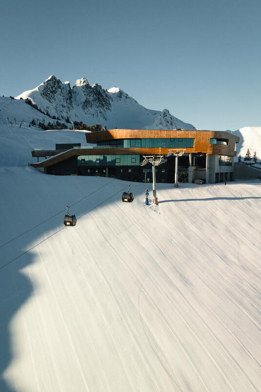 Bergstation am Spieljoch mit modernem Gebäude und Seilbahn, umgeben von schneebedeckten Bergen und klar blauem Himmel.