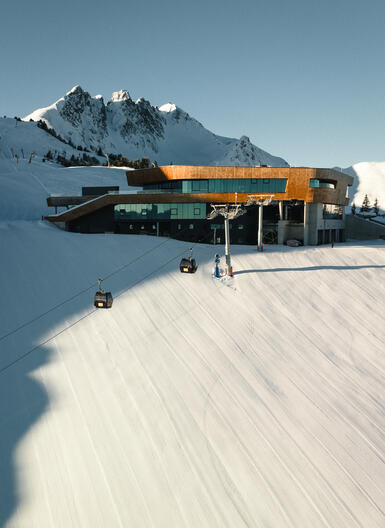Bergstation am Spieljoch mit modernem Gebäude und Seilbahn, umgeben von schneebedeckten Bergen und klar blauem Himmel.