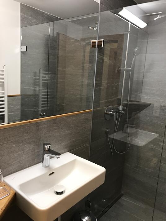 Modernes Badezimmer mit Glasdusche, Waschbecken und schlichten grauen Fliesen.