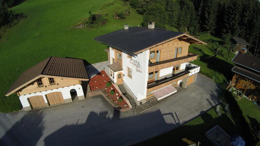 Luftaufnahme des Ferienhauses Zeller am Stummerberg mit angrenzender Garage in einer grünen Landschaft.