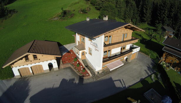 Luftaufnahme des Ferienhauses Zeller am Stummerberg mit angrenzender Garage in einer grünen Landschaft.