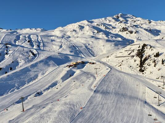 Schneebedeckte Berglandschaft mit Skipisten und einer Hütte im Skigebiet Hochzillertal. Im Hintergrund majestätische Berge unter klarem blauem Himmel. Seilbahnen sind sichtbar, die an den Berghang führen. Die Pisten sind frisch präpariert und laden zum Skifahren ein.