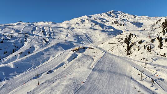 Schneebedeckte Berglandschaft mit Skipisten und einer Hütte im Skigebiet Hochzillertal. Im Hintergrund majestätische Berge unter klarem blauem Himmel. Seilbahnen sind sichtbar, die an den Berghang führen. Die Pisten sind frisch präpariert und laden zum Skifahren ein.