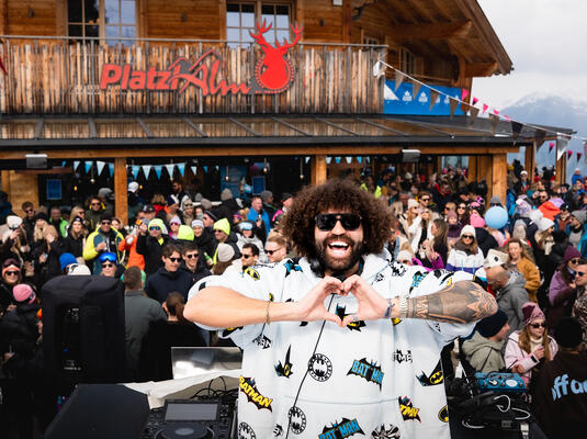 DJ macht Herzzeichen vor einer großen Menge auf der PlatzlAlm beim Event Alpicon. Festliche Atmosphäre.