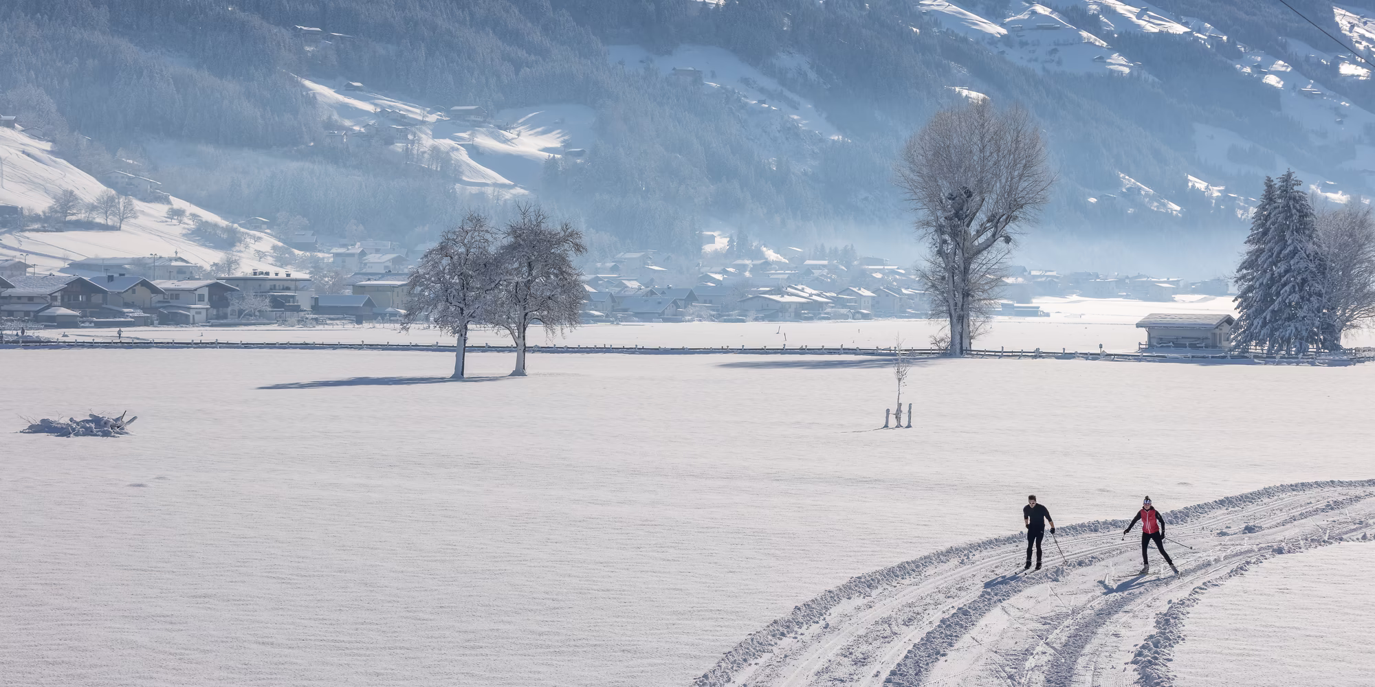 Zwei Personen, die im Zillertal auf einer Langlaufstrecke langlaufen umgeben von Schnee an einem sonnigen Wintertag
