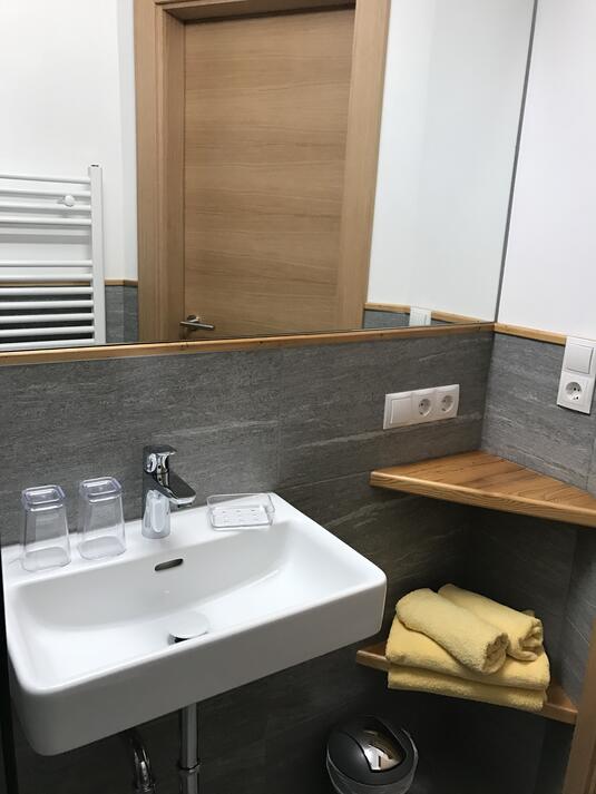 Badezimmer mit Waschbecken, Handtüchern, Spiegel und Holzregal.