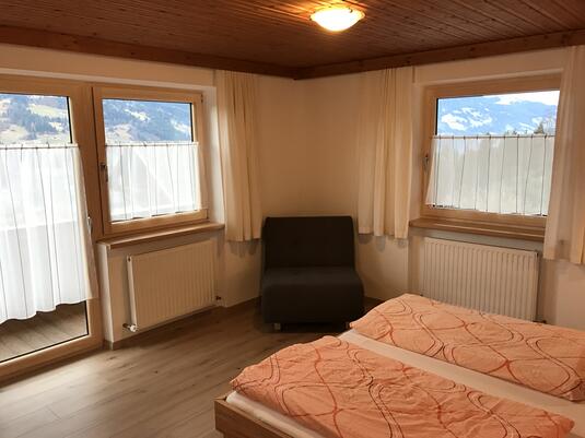 Helles Zimmer mit zwei Fenstern, einem Doppelbett und einem Sitzbereich mit Ausblick auf die Landschaft.