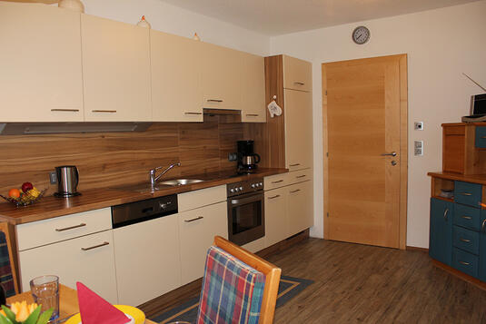 Moderne Küche in der Ferienwohnung mit Holzregalen, Geräten und einem Tisch mit Stühlen im Vordergrund.