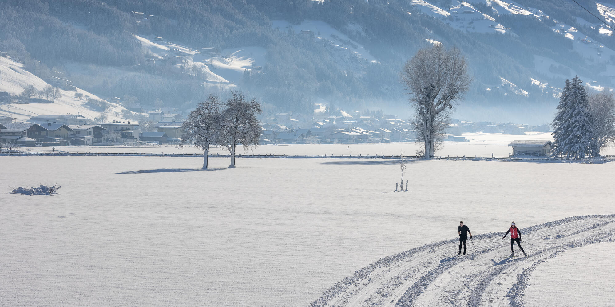 Zwei Personen, die im Zillertal auf einer Langlaufstrecke langlaufen umgeben von Schnee an einem sonnigen Wintertag
