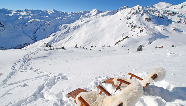 Ein Blick auf schneebedeckte Berge mit zwei Liegen im Vordergrund, Himmel ist klar und blau.