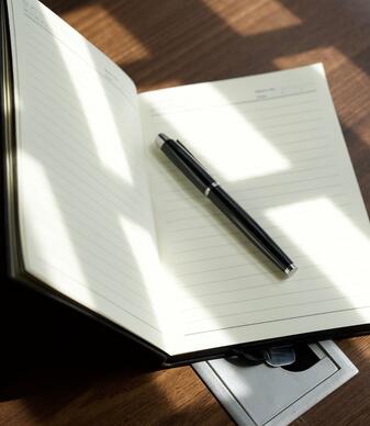Ein offenes Notizbuch mit einer schwarzen Füllfederhalter auf einem Holztisch, Sonnenlicht fällt darauf.