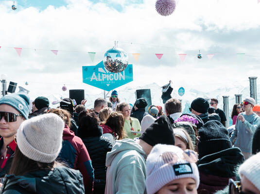 Menschen feiern auf dem Event Alpicón im Zillertal, umgeben von Musik und bunten Dekorationen auf der Kristallhütte.